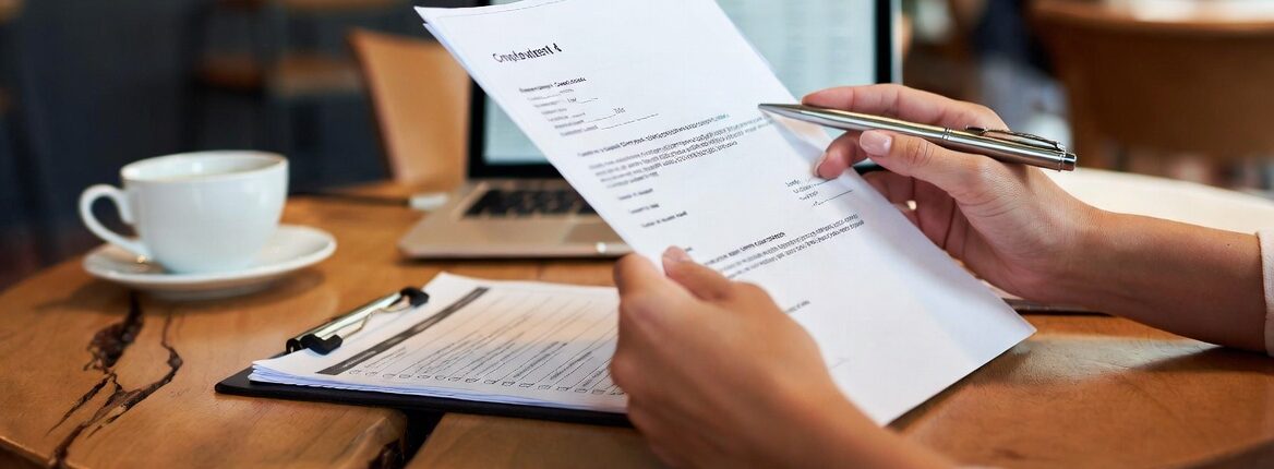 Gros plan sur les mains d'une personne vérifiant des contrats de travail et une check-list de conformité sociale sur la table d'un café, en préparation d'un contrôle éclair Horeca. 